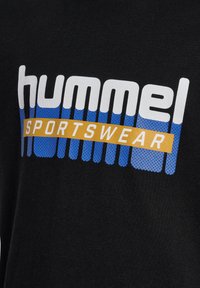 Sort bomulds T-shirt med "hummel" i hvid og blå tekst, samt "SPORTSWEAR" i gul på et mønstret baggrund.