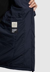 Wnętrze granatowej kurtki, charakteryzujące się gładką teksturą, metką z napisem "Zrobione z miłością" oraz dodatkową czarną metką marki.