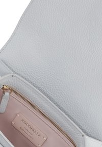 Borsa a mano in pelle bianca con finitura testurizzata, dotata di una tasca con zip interna di un delicato rosa, e dettagli metallici dorati.