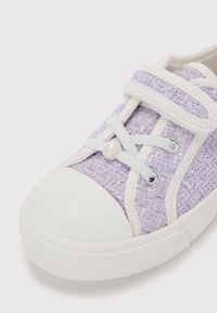 Sneaker din țesătură lavandă cu o suprafață texturată, vârf din cauciuc alb și curea Velcro, având o aplicație decorativă cu perle.