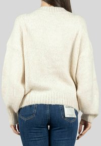 Maglione lavorato a maglia di un morbido beige chiaro con una vestibilità rilassata, collo e orlo a coste e maniche oversize, abbinato a jeans attillati blu scuro.