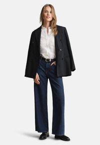 Juodas dvieilis švarkas, balta mygtukais užsegama palaidinė ir tamsiai mėlyni plačiakelniai džinsai, derinami su juodais batais, pasižymintys klasikiniu dizainu.