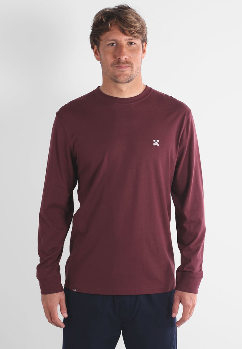 T-shirt en coton bordeaux à manches longues avec col rond et logo blanc sur la poitrine gauche. Texture lisse, coupe décontractée.