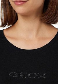 T-shirt nera a girocollo con logo "GEOX" testurizzato in colore a contrasto. Il tessuto appare morbido e liscio, adatto per un abbigliamento casual.