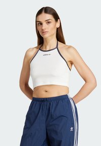 Vitt kort halterneck-top i mjukt tyg, med blåa detaljer och en minimalistisk adidas-logga i mitten.