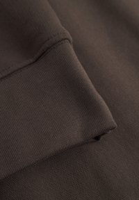 Bovenstuk van een bruine hoodie met een gladde textuur en geribbelde zoomdetails. Het materiaal lijkt dik en warm, geschikt voor casual kleding.