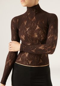 Top a collo alto in pizzo marrone con maniche lunghe, caratterizzato da un motivo floreale e una vestibilità aderente, abbinato a una gonna nera.