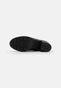 Suela de goma negra con un patrón de banda de rodadura profundo, con un ligero tacón y un material superior negro en contraste. Textura suave con líneas definidas.
