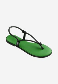 Sandaletto piatto verde con cinturini elastici neri, caratterizzato da un design minimalistico e una soletta liscia e testurizzata. I dettagli includono un occhiello all'alluce.