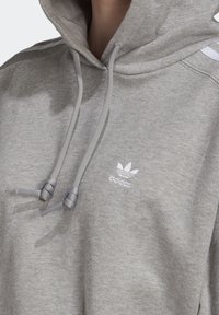 Grå bomullshuvtröja med dragsko i huvan, med en liten vit Adidas-logotyp och matchande grå dragskor framtill.