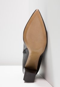 Zapato de cuero negro con punta afilada y un tacón bloque de altura media. La suela es lisa con un leve patrón de agarre texturizado.