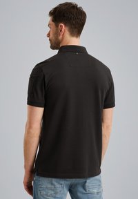 Zwarte polo met een kraag, korte mouwen en een borstzak; gladde textuur; heeft een lus detail aan de achterkant.