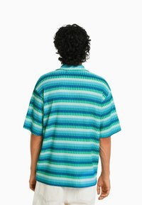 Kortärmad skjorta med horisontella ränder i olika nyanser av blått och grönt. Materialet har en ribbad struktur och en krage.