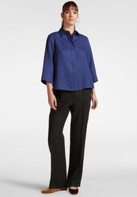 Blusa di lino blu navy con colletto a punta, maniche a tre quarti e taglio dritto, abbinata a pantaloni neri a gamba larga e ballerine marroni.