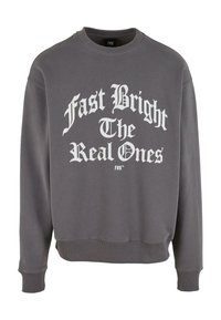 Grå genser med rund hals, ribbestrikkede mansjetter og fald. Har stor hvit tekst: "Fast Bright The Real Ones" på forsiden.