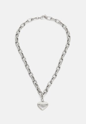 Silberne Kette mit einem herzförmigen Anhänger, eingraviert mit dem Wort „GUESS“, zentriert auf weißem Hintergrund.
