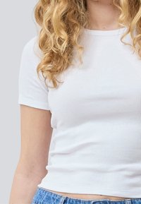 Weißes, geripptes Baumwoll-T-Shirt mit kurzen Ärmeln, taillierter Passform und rundem Ausschnitt, kombiniert mit blauen Denim-Shorts.
