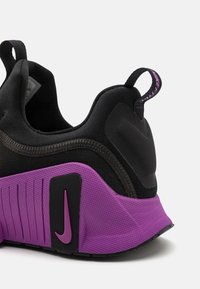 Adidași atletici negri și purpurii, cu o talpă texturată, materiale contrastante și un logo Nike proeminent în purpurie pe călcâi.