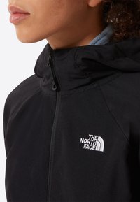 Gros plan d'une personne portant une veste noire The North Face avec une fermeture éclair à l'avant et un col haut couvrant le cou.