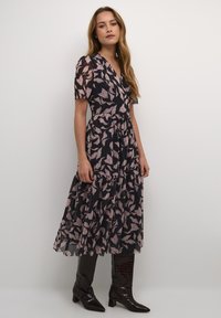 Abito fluido blu navy con motivo a foglie rosa, scollo a V, maniche corte e gonna a strati, abbinato a stivali neri lucidi al ginocchio.