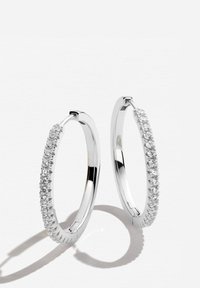 Silverörhängen i form av ringar med en texturerad yta och en rad klara, runda stenar på ena sidan. Polerad finish med gångjärnsstängning.