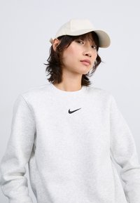 Witte pet en lichtgrijze sweatshirt met een klein zwart Nike-logo. De stof lijkt zacht en textuur te hebben, met een ronde hals.
