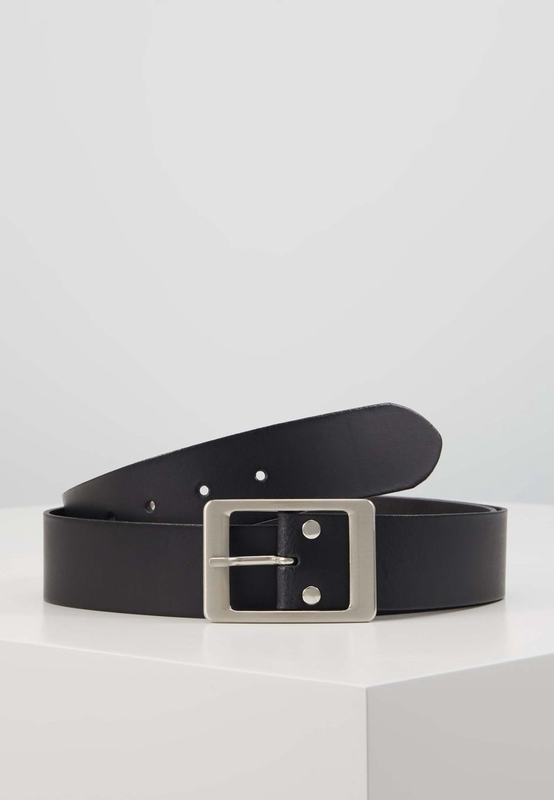Ceinture en cuir noir avec une boucle rectangulaire en métal argenté, présentée enroulée sur une surface blanche sur un fond gris uni.
