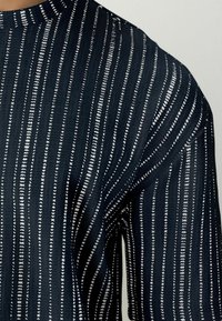 Navy blue sweater featuring horizontal white stripes with a textured knit pattern, showcasing a modern design and a round neckline.