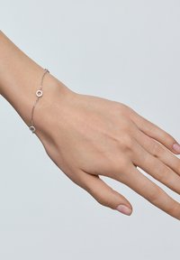 Srebrna bransoletka łańcuszkowa z okrągłymi akcentami, z małymi okrągłymi detalami. Smukły design na szczupłym nadgarstku na neutralnym tle.