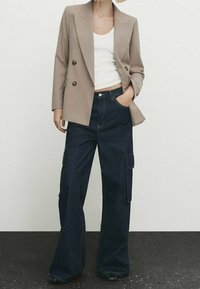 Blazer beige croisé porté sur un débardeur blanc, associé à un jean cargo bleu marine à jambes larges avec poches latérales et coupe décontractée.