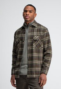 Flanellen overhemd in donkergroen ruitpatroon met witte en bruine accenten, voorzien van twee borstzakken en een knoopsluiting. D gedragen over een gestructureerde grijze trui.