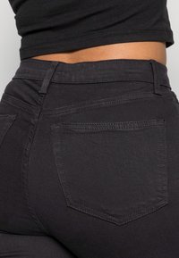 Jeans de mezclilla negra con un diseño ajustado, que cuentan con bolsillos traseros, detalles de costura sutiles y una tela lisa y texturizada.