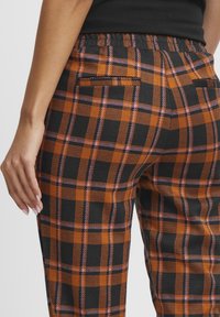 Women's plaid pants in orange, black, and pink. Features an elastic waistband, back pockets, and a smooth, soft texture.