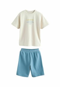 T-shirt crème à manches courtes avec impression graphique, associée à un short côtelé bleu clair avec une taille élastique. Tissu et design confortables.