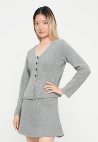 Szary sweter robiony na drutach z długimi rękawami, dekoltem w serek, pięcioma czarnymi guzikami i pasującą spódnicą; miękka tekstura, prosty design, casualowy krój.