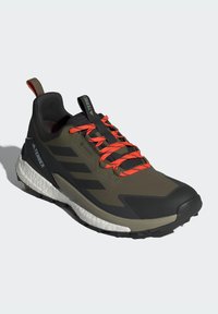 Terrex trail running shoe in dark olive and black with bright orange laces. Features a textured upper, cushioned sole, and rugged tread design.