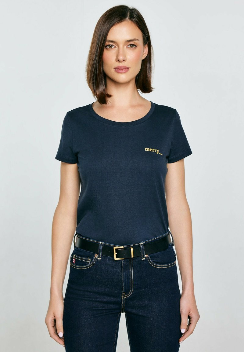 Námořnická modrá bavlněná tričko s kulatým výstřihem a vyšitým nápisem "merry" zlatou barvou. V kombinaci s tmavými denimovými džíny a černým opaskem.