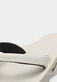 Κοντινή λήψη ενός μπεζ σαγιονάρου με λουράκι ενίσχυσης και λογότυπο Nike στο πλάι της σόλας.