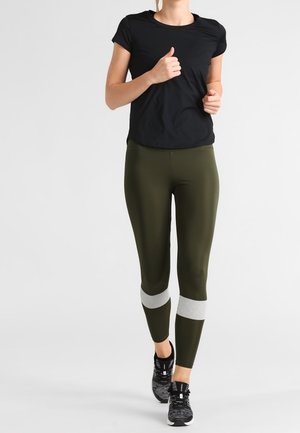 T-shirt de sport à manches courtes noir associé à des leggings vert olive avec des accents en maille blanche. Porté avec des baskets noires.