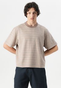Tricou rayé în nuanțe de bej și brun, cu mâneci scurte, guler rotund și o croială lejeră, fabricat dintr-un material moale.