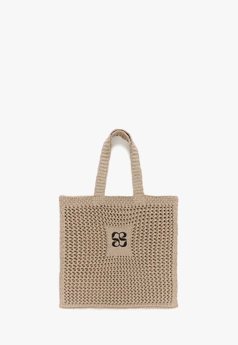 Sac fourre-tout en crochet beige avec deux anses et un motif floral abstrait noir central sur fond blanc.