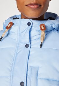 Giacca a collo alto in nylon blu chiaro con imbottitura, caratterizzata da cuciture a vista e cordini in pelle con texture intrecciata.