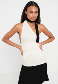 Top halter canelado em creme e preto, com uma alça única no ombro. O design apresenta uma silhueta ajustada e um tecido texturizado.