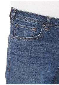 Jeans in denim blu scuro con un classico design a cinque tasche, caratterizzati da cuciture a contrasto e una chiusura con zip. La superficie è liscia con leggere sfumature.