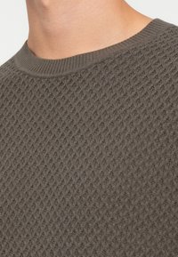 Suéter de punto texturizado en gris oscuro, con un cuello redondo y un patrón de diamantes en relieve. Tejido suave con un cuello ligeramente estirado.