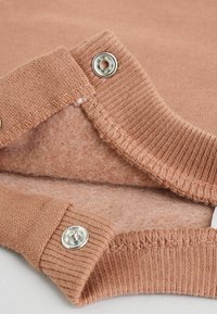 Perzikkleurige gebreide sweaterkraag met ribbelstructuur, voorzien van zilveren drukknoopjes en een zachte binnenvoering. Close-up view.
