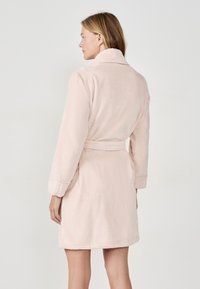 Ljust rosa badrock i mjukt, texturerat tyg, med långa ärmar, krage och ett knytbälte i midjan.