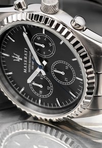 Maserati-klocka med boett i rostfritt stål, svart urtavla, silvermarkeringar, tre sub-dialer och en strukturerad bezel. Vattentålig upp till 100 meter.