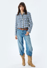 Blå och vit rutmönstrad skjorta med knappar och två framfickor, kombinerad med högmidjade ljusblå jeans och bruna cowboystövlar.