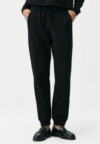 Czarne spodnie dresowe z regulowanym sznurkiem w talii, zwę�żanymi mankietami i bocznymi kieszeniami, wykonane z miękkiego, gładkiego materiału dla komfortu.